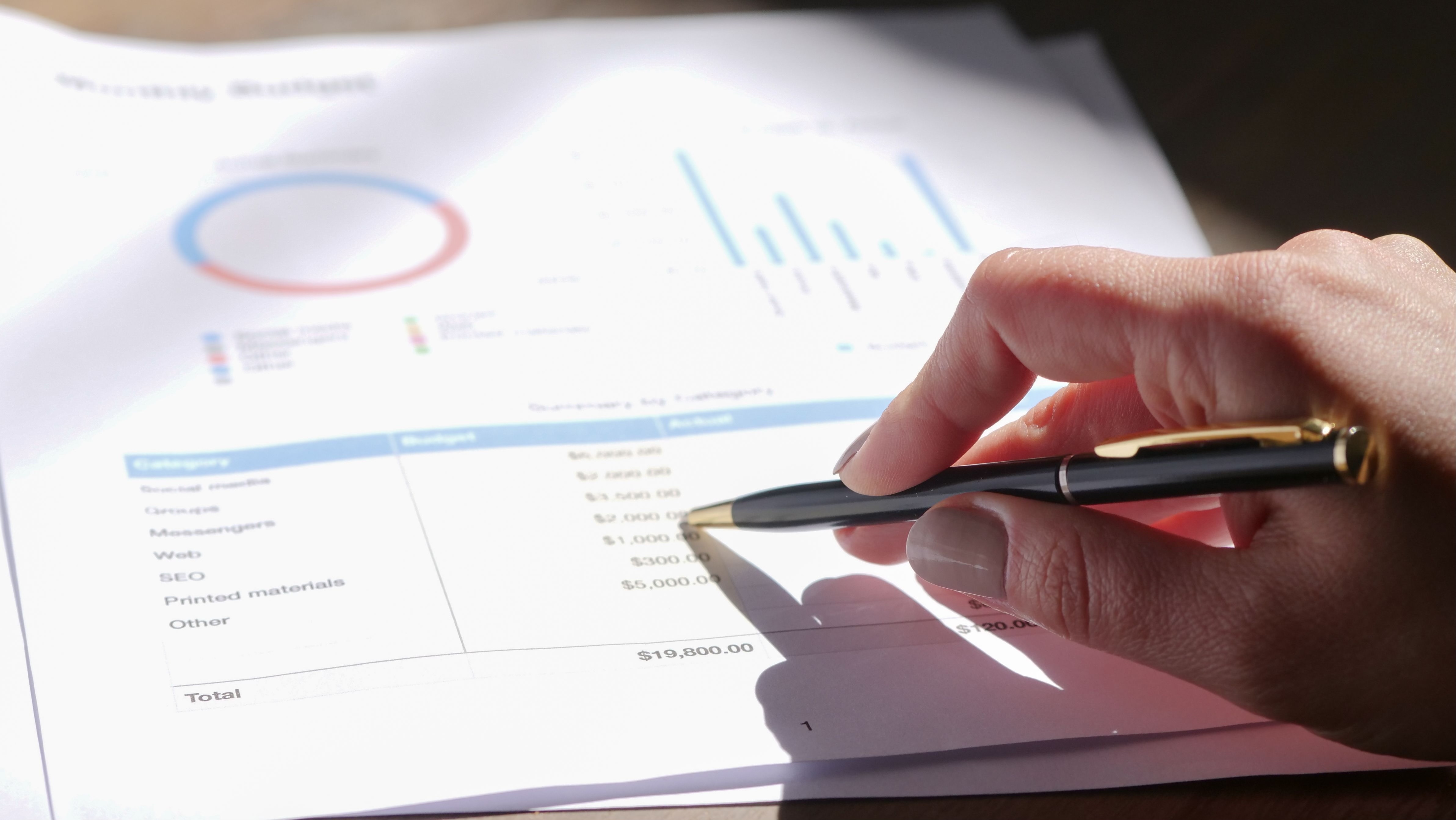 A hand holding a pen checks printed tables and charts in a data report.